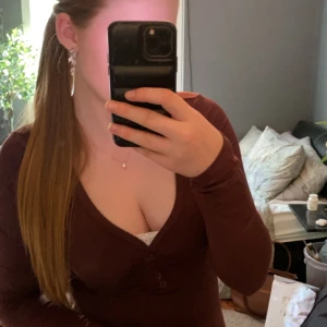 Brun långärmad v-ringad topp - Säljer en brun långärmad topp med v-ringning och knappar framtill. Toppen har en figurnära passform och är perfekt för dig som gillar en enkel men stilren look.