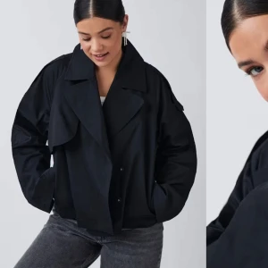 Svart croppad kavajjacka - Säljer en svart croppad trenchcoat med bred krage och dubbelknäppning. Jackan har långa ärmar och en boxig, oversized passform. Perfekt för dig som vill ha en stilren och trendig look. Oanvänd. 