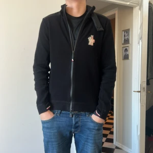 Svart fleecejacka från Moncler - Säljer en svart fleecejacka från Moncler med dragkedja framtill och diskret logga på bröstet. Jackan har hög krage och ribbade muddar vid ärmslut och nederkant. Perfekt för kyliga dagar. Nypris ca 6000 på Nk, mitt pris 2500. **ÄKTA**