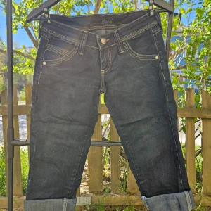 Mörkblå jeansbyxor från Crackpot - Säljer ett par mörkblå jeansbyxor från Crackpot med kontrastsömmar och klassisk femficksdesign. Byxorna har uppvikta benslut och knappgylf. Perfekta för en avslappnad stil.