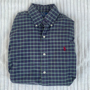 Rutig skjorta från Polo Ralph Lauren - Säljer en grön och blå rutig skjorta från Polo Ralph Lauren i slim fit. Skjortan har långa ärmar, klassisk krage och knappar framtill. Broderad röd logga på bröstet. Perfekt för dig som gillar stilrena och klassiska plagg.