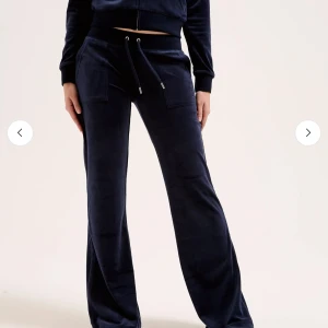 Mörkblå velourbyxor från Juicy Couture - Mörkblå mjukisbyxor från Juicy Couture i mjuk velour med bred resår i midjan och dragsko. Byxorna har raka, vida ben och fickor fram samt bakficka med knappar. Storlek xs, använd fåtal gånger så dom är i nyskick 