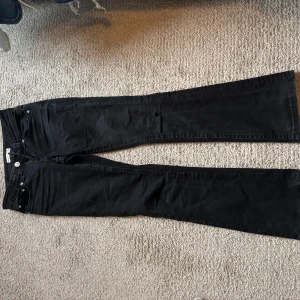 Svarta bootcut jeans - Säljer ett par svarta jeans med bootcut-modell. Klassisk femficksdesign och knappgylf. Jeansen har en något utsvängd passform nedtill och är tillverkade i ett mjukt denimtyg.