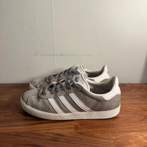Grå Adidas Gazelle sneakers - Säljer ett par grå Adidas Gazelle sneakers i mocka. Skorna är i bra skick förutom de små markerna på trå området. Perfekt nu till sommaren.