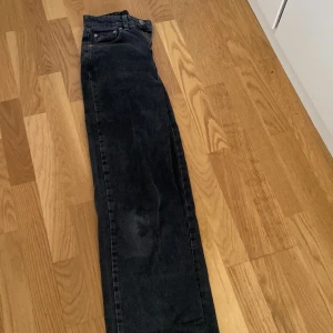 Svarta raka jeans med rå kant - Säljer ett par svarta jeans med rak passform och rå, fransig kant nertill. Klassisk femficksmodell med silverfärgade nitar och bälteshällor. Jeansen har en något tvättad look och är perfekta för en avslappnad stil.