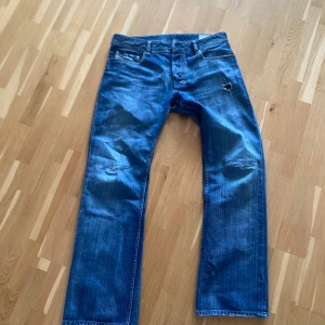 Blå jeans från Diesel - Säljer ett par blå jeans från Diesel, modell Zatiny. De har en klassisk femficksdesign med slitna detaljer och en liten reva på ena benet. Perfekta för en avslappnad stil.