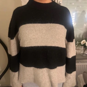 Randig stickad tröja från Gina Tricot - Säljer en mysig stickad tröja från Gina Tricot i svart och grå/brun. Tröjan har ett randigt mönster och långa ärmar. Perfekt för kyliga dagar!