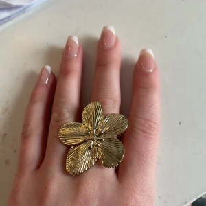 Guldfärgad blomformad ring - Äkta edblads blomning Säljer en unik guldfärgad ring formad som en blomma med detaljerade kronblad. Perfekt för att ge en elegant touch till din stil. Justerbar storlek för att passa de flesta fingrar. Säljs för den är för stor, aldrig använd. Nyligen köpt❤️