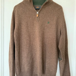 Brun tröja från Morris - Säljer en stilren brun tröja från Morris med dragkedja och ribbad krage. Grön detaljer på ärmarna. Storlek M. Bra skick.
