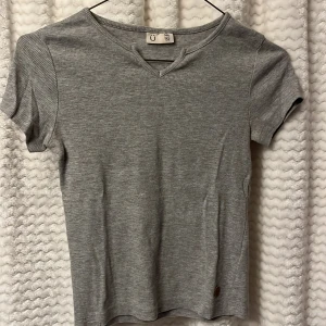 Grå ribbad topp från Kappahl. 🩶 - Säljer en stilren grå ribbad topp från Kappahl.  Den har en v-ringad hals och korta ärmar. 🐨