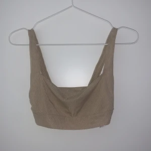 Beige ribbad topp från Nelly - Snygg beige ribbad topp från Nelly. Toppen har breda axelband och en stilren design som passar perfekt till både jeans och kjol. Perfekt för en trendig look!