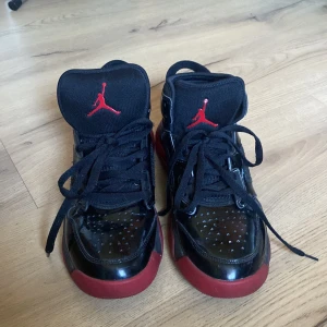 Svarta och röda Nike Air Jordans - Säljer ett par svarta och röda Nike Air Jordans med klassisk snörning och ikonisk logga. Skorna har en blank yta och är perfekta för dig som vill ha en stilren look med en sportig touch.