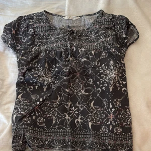 Mönstrad blus med knyt - Säljer en snygg mönstrad blus från Odd Molly i svart och vitt med inslag av rosa. Blusen har korta ärmar och ett knytband vid halsen för en extra detalj. Perfekt för en stilren look!