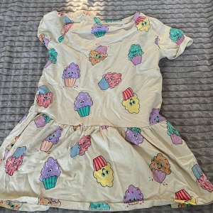 Färgglad klänning med glassmotiv - Söt klänning med ett lekfullt mönster av färgglada glassar i olika nyanser. Klänningen har korta ärmar och en avslappnad passform, perfekt för sommarens varma dagar.