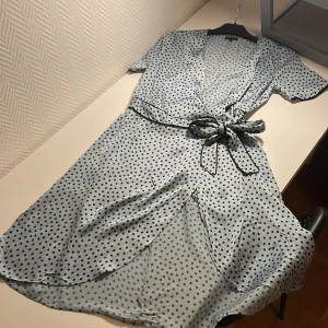 Klänning - Blå siden omlottklänning med svarta prickar. Knytband i midjan. V-ringad. Superfin och bra kvalitet! 