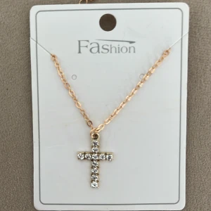 Rostfritt Guldhalsband med korshänge - Rostfritt och elegant guldhalsband med ett glittrande korshänge. Hänget är dekorerat med klara stenar som ger en lyxig känsla. Perfekt för att lägga till en touch av glamour till din outfit.