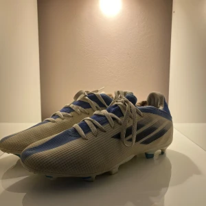  fotbollsskor  - Snygga fotbollsskor från Adidas i vitt och blått. Skorna har en modern design med snörning och en slitstark sula för bra grepp på planen. Perfekta för fotbollsträning och matcher. De är andvända men inte synligt