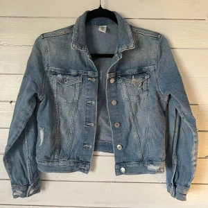Blå jeansjacka från &Denim - Säljer en blå jeansjacka från Jackan har en normal passform med knappar framtill och två bröstfickor med knappar. Perfekt för en avslappnad stil.