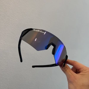 Sportiga solglasögon från TechFit Gear - Snygga sportglasögon från TechFit Gear med en futuristisk design. De har en spegelblå lins och svarta bågar, perfekt för utomhusaktiviteter. Glasögonen har en omslutande passform som ger bra skydd mot solen.