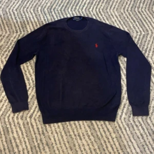 Ralph Lauren stickad tröja - Säljer en stilren mörkblå tröja från Ralph Lauren i mjuk bomull. Tröjan har en klassisk rund hals och långa ärmar. Den är dekorerad med Ralph Laurens ikoniska röda logotyp på bröstet. Perfekt för en avslappnad men elegant look. Tveka inte på att höra av dig vid minsta lilla fundering!💛