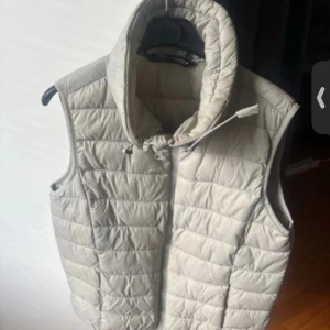 Beige quiltad dunväst - Snygg beige quiltad dunväst från Zara. Perfekt för lager-på-lager under kyliga dagar. Västen har en hög krage och dragkedja framtill för extra värme och stil.