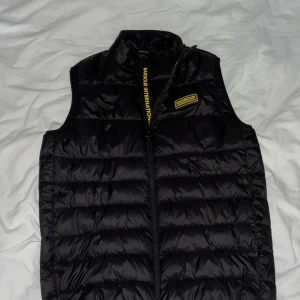 Svart dunväst från Barbour International - Säljer en snygg svart dunväst från Barbour International. Västen har en dragkedja framtill och ett stilrent märke på bröstet. Inte använt den nått så den e helt ny. Jag e 181 o den sitter bra på mig. Priset kan diskuteras