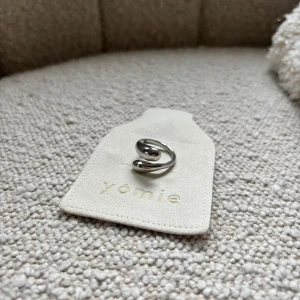 Silverfärgad ring från Yomie - Elegant silverfärgad ring från Yomie med en modern och stilren design. Ringen har en öppen form som ger en unik touch. Perfekt för att komplettera din look med en subtil men chic detalj.