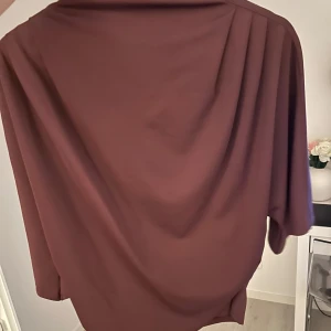 Vinröd klänning - Elegant vinröd topp med draperad design. Perfekt för en stilfull kväll. Toppen har en mjuk och flödande passform som ger en vacker siluett.
