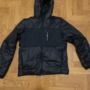 Svart vindjacka med huva - Säljer en stilren svart vindjacka med huva. Jackan har en dragkedja framtill och är långärmad. Perfekt för blåsiga dagar. Sail racing 