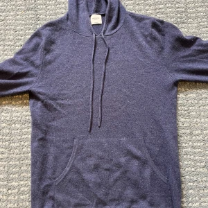 Kashmir hoodie från John Henric - Säljer en lyxig mörkblå hoodie i 100% cashmere från John Henric. Tröjan har en klassisk design med känguruficka och justerbar huva med snören. Perfekt för en stilren och bekväm look.