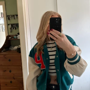 Grön och beige baseball jacka - Snygg baseball jacka i grönt och begie med röda bokstäver på fram och baksidan. Jackan har begiea ärmar och kan stängas med knappar. Perfekt jacka för vår och sommar☀️🍀 Använd fåtal gånger!!