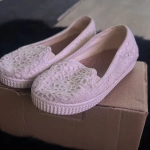 Vita spetsiga loafers från Zara - Säljer ett par vita loafers från Zara med vacker spetsdesign. Skorna har en platt sula och är perfekta för en elegant och bekväm stil. De är lätta att matcha med olika outfits och ger en romantisk touch.
