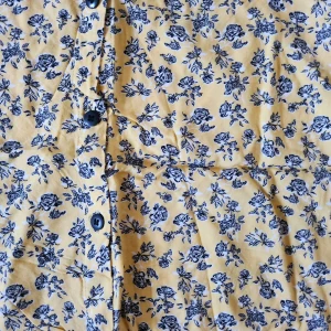 Gul blommig kjol med knappar - Charmig gul kjol med svart blommönster och knappar framtill. Perfekt för en solig dag!