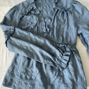 Blå blus från NAKD - Superfin o nice blå blus från NAKD har en v-ringning och volanger både framtill och på ärmarna. Superfin till både vår och sommar