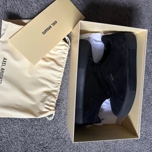 Svarta sneakers från Axel Arigato - Snygga svarta sneakers från Axel Arigato i mocka. Skorna har en stilren design med en diskret logga på sidan och en matchande svart sula. Perfekta för en minimalistisk look. Skorna är i nyskick, endast använda ett fåtal gånger!