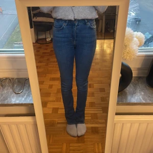 Blå bootcut jeans - Säljer ett par snygga blå bootcut jeans med hög midja. De har en klassisk femficksdesign och är perfekta för en avslappnad stil. Jeansen är tillverkade i ett bekvämt denimtyg som ger en skön passform.