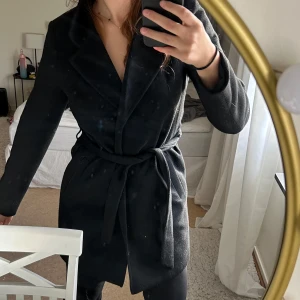 Svart kappa med bälte - Snygg svart kappa med bälte i midjan för en elegant look. Perfekt för kyligare dagar med sin långa design och klassiska krage. Från vero Moda storlek M.