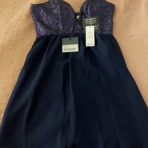 Mörkblå klänning med paljetter från Nelly - Snygg mörkblå klänning från Nelly med glittrig paljettöverdel och tunna axelband. Perfekt för festliga tillfällen. Klänningen har en elegant passform och en vacker fallande kjol.