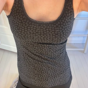 Svart linne med spetsdetaljer - Snyggt svart linne från H&M Young med små vita cirklar och spetsdetaljer vid halsringningen samt längst ner. Linnet har en bekväm passform och ärmlös design.