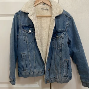 Blå jeansjacka med teddyfoder - Säljer en snygg blå jeansjacka från H&M med mjukt vitt teddyfoder. Jackan har långa ärmar och knappar framtill samt på bröstfickorna. Perfekt för kyligare dagar! 🧥