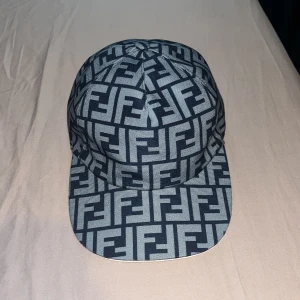 Mönstrad keps med logotyp från Fendi - Snygg keps från Fendi med ett iögonfallande mönster av logotyper i blått och grått. Perfekt för att ge din outfit en trendig touch. Justerbar passform för optimal komfort.
