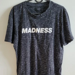 Svart t-shirt från Reserved med text - Säljer en svart t-shirt från Reserved med vit text 'MADNESS' på framsidan. T-shirten har en melerad design och korta ärmar. Perfekt för en avslappnad stil.