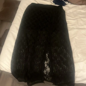 Svart spetskjol från Michael Kors - Snygg svart långkjol i spets från Michael Kors. Perfekt för en elegant look med sin genomskinliga spetsdesign. Kjolen har en elastisk midja för bekväm passform. Ett måste för garderoben!