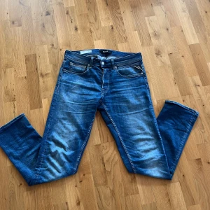 Blå jeans från Replay - Snygga blå jeans från Replay med en klassisk femficksdesign och lätt slitna detaljer. De har en knappgylf och är perfekta för en avslappnad stil. Passformen är slim/straight och de är tillverkade i ett bekvämt denimtyg. Nypriset ligger på runt 1800