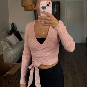Ljusrosa omlottopp med knyt - Ljusrosa omlottopp i ribbat material med långa ärmar och knyt i midjan. Står tyvärr ej vad det är för storlek men skulle säga att den sitter som en S.