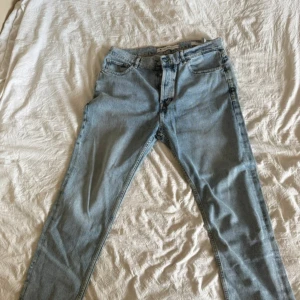 Guess Relaxed James ljusblå jeans Strl W34 - Ljusblå jeans från Guess, modell Relaxed James, med avslappnad passform och raka ben. Klassisk femficksdesign, knappgylf och snygg tvättad denim. Perfekta för en chill och stilren look. Materialet är bomull och jeans.