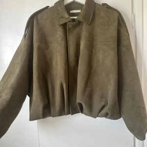 Olivgrön mockajacka från Zara - Säljer en trendig olivgrön mockajacka från Zara med oversized passform och coola axeldetaljer. Jackan har dragkedja framtill, klassisk krage och långa ärmar. Som ny, bara använd ett fåtal gånger!😇