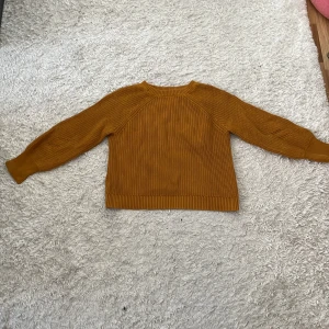 Senapsgul stickad tröja med mönster - Mysig senapsgul stickad tröja med lång ärm och ribbade muddar. Tröjan har snygga stickade detaljer på bröstet och ärmarna samt en något längre bakdel. Perfekt för lager-på-lager och chill höst- och vinterstil.