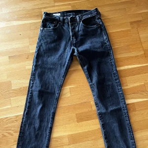 Levi's 501 svarta jeans W28 L32 - Säljer ett par klassiska svarta Levi's 501 jeans i rak modell. Jeansen har fem fickor, knappgylf och snyggt mörkt tvättad denim. Perfekta för dig som gillar tidlös stil och vill ha ett par jeans som funkar till allt.
