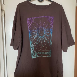 Brun oversized t-shirt - Cool brun oversized t-shirt med färgstarkt tryck framtill i lila och blått med sol- och månmotiv samt texten 'The Dreamer'. Skön passform och lite längre ärmar, perfekt för en avslappnad stil. Frakt tillkommer